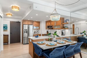 A modern kitchen with wooden cabinets, a stainless steel refrigerator, and a central island with a sink. - Luxurious Ocean View Condo Steps to Kaanapali Beach -Whaler 807 (Lahaina)