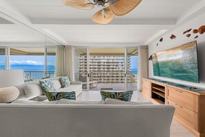 Een moderne woonkamer met een grote televisie, een bank en een balkon met uitzicht op zee.