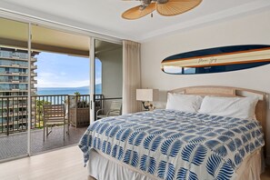 Habitación de hotel con cama, ventana grande, balcón y vistas al océano, además de ventilador de techo.