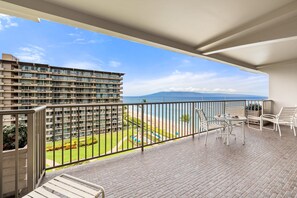 Ein Balkon mit Blick auf Strand und Meer, ein Schwimmbecken sowie ein mehrstöckiges Gebäude.