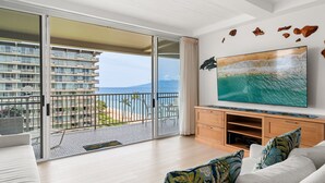 Una habitación con un gran ventanal corredera que da a un balcón con vistas a un edificio y al océano.