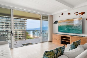 Ein Zimmer mit einer großen Schiebeglastür, die auf einen Balkon mit Blick auf ein Gebäude und das Meer führt.