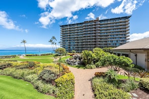 A multi-story hotel with a view of the ocean, surrounded by landscaped gardens and a pathway. - Luxurious Ocean View Condo Steps to Kaanapali Beach -Whaler 807 (Lahaina)