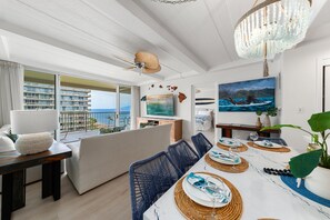 Un comedor moderno con una mesa blanca, sillas azules y vistas al océano a través de amplios ventanales.