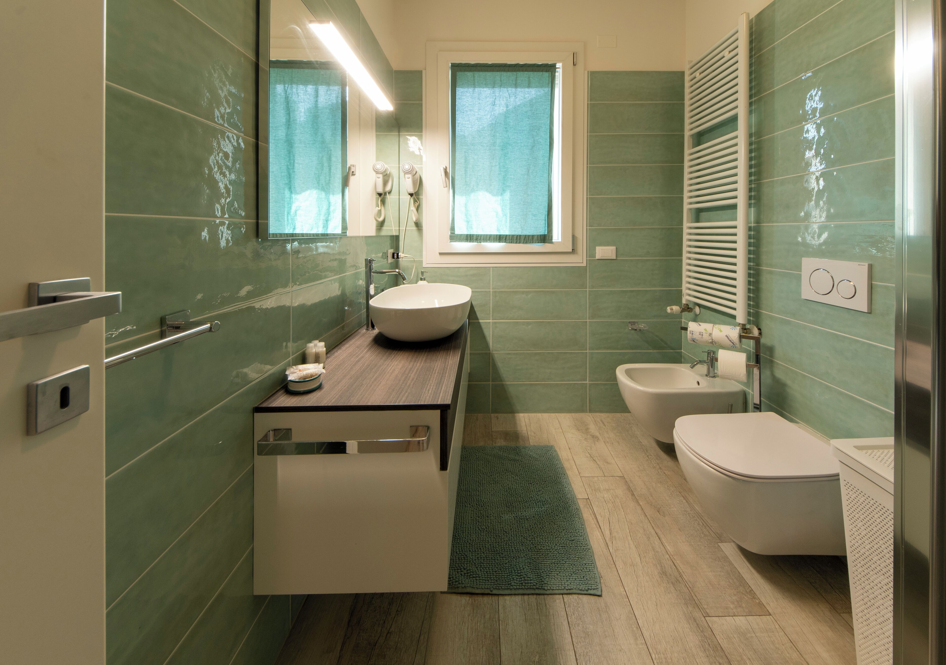 Une salle de bain comprenant un lavabo, des toilettes et un bidet, un miroir et une fenêtre.