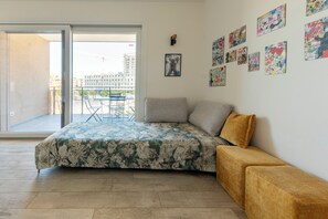 A bedroom with a bed, a sofa, a balcony with a table and chairs, and various artworks on the wall. - HouSmart Greta Garbo 12 (Bologna)