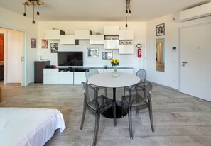 A modern kitchen with white cabinets, a flat-screen TV, and a dining area with a round table and chairs. - HouSmart Greta Garbo 12 (Bologna)
