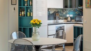 Una cocina moderna con encimera blanca, un mueble de estanterías color turquesa y un jarrón con flores amarillas sobre una mesa.