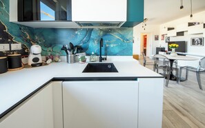 A modern kitchen with a built-in island, a black sink, and a teal backsplash. - HouSmart Greta Garbo 12 (Bologna)