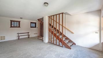 A room with a stone floor, a wooden bench, a staircase with wooden railings, and two windows with wooden frames.