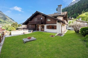 A two-story wooden house with a balcony, a stone pathway, and a well-maintained lawn. - Family Apartment Steps From Ski Lifts (Courmayeur)