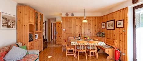 A wooden interior with a sofa, dining table, chairs, and a fire extinguisher.