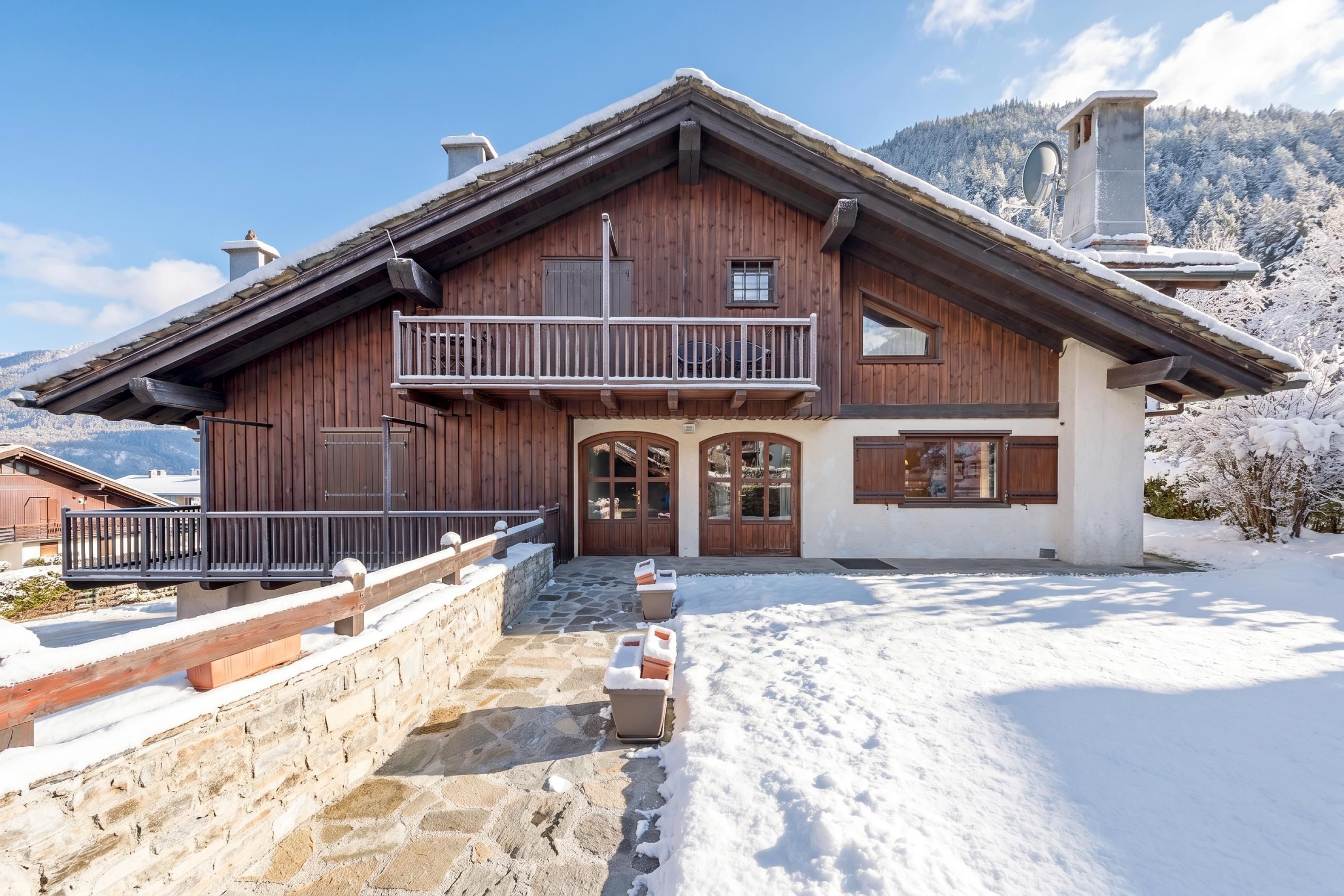 Un chalet en bois doté d’un balcon, d’un escalier en pierre et surplombant un paysage enneigé.