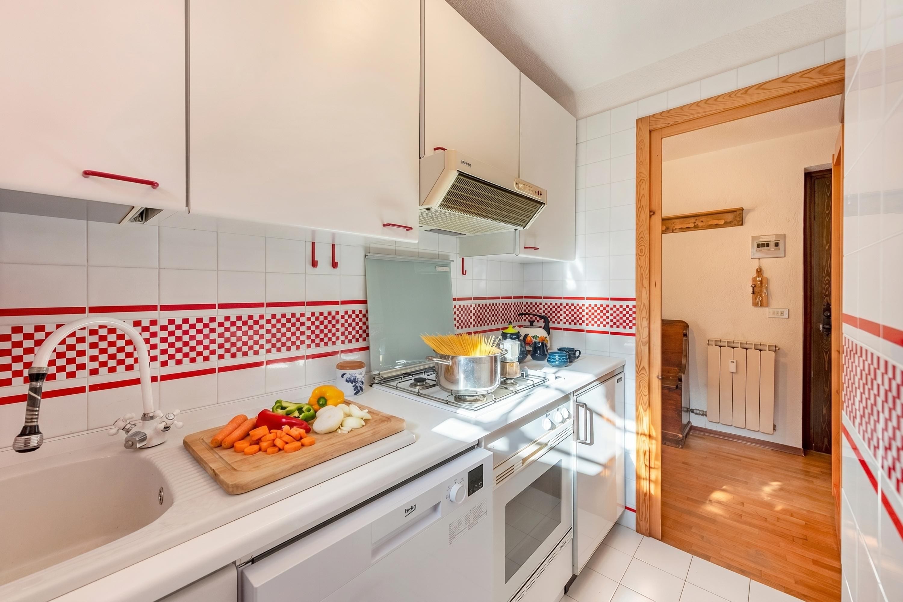 A modern kitchen with white cabinets, a stainless steel stove, and a red and white checkered backsplash.