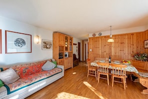 A cozy room with a sofa, wooden cabinets, a dining table with chairs, and a kitchen area. - Family Apartment Steps From Ski Lifts (Courmayeur)