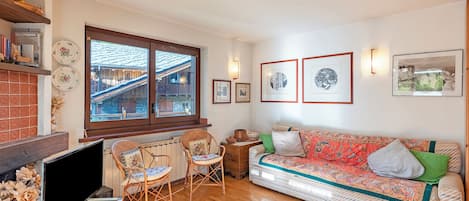 Un salon comprenant un canapé, des fauteuils, un téléviseur, une cheminée et une fenêtre donnant sur un immeuble.