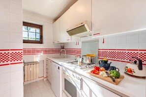 Una cocina con armarios blancos, una ventana, una estufa y una encimera con verduras.