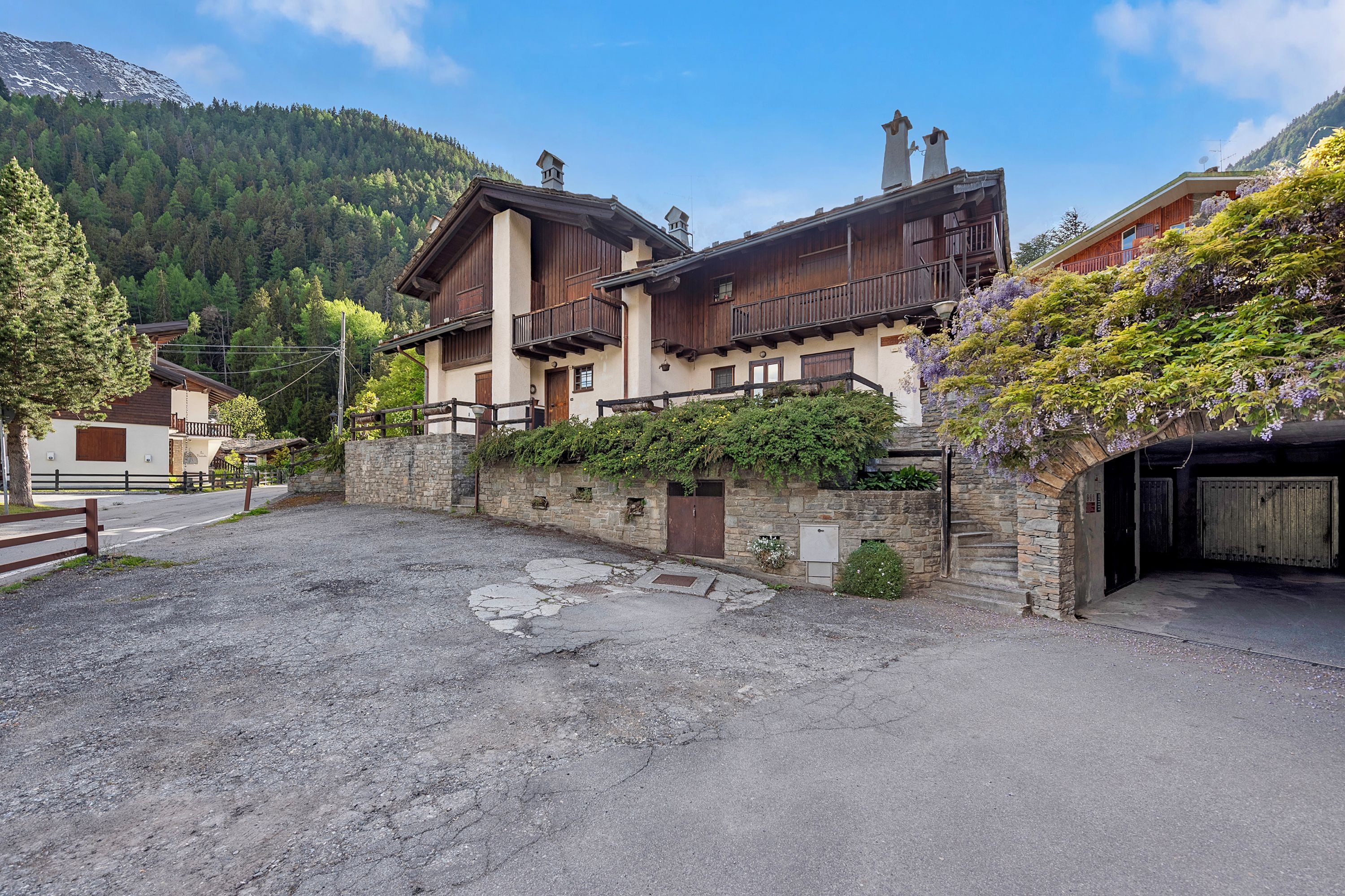 A traditional chalet-style building with a stone facade, wooden balconies, and a paved courtyard.
