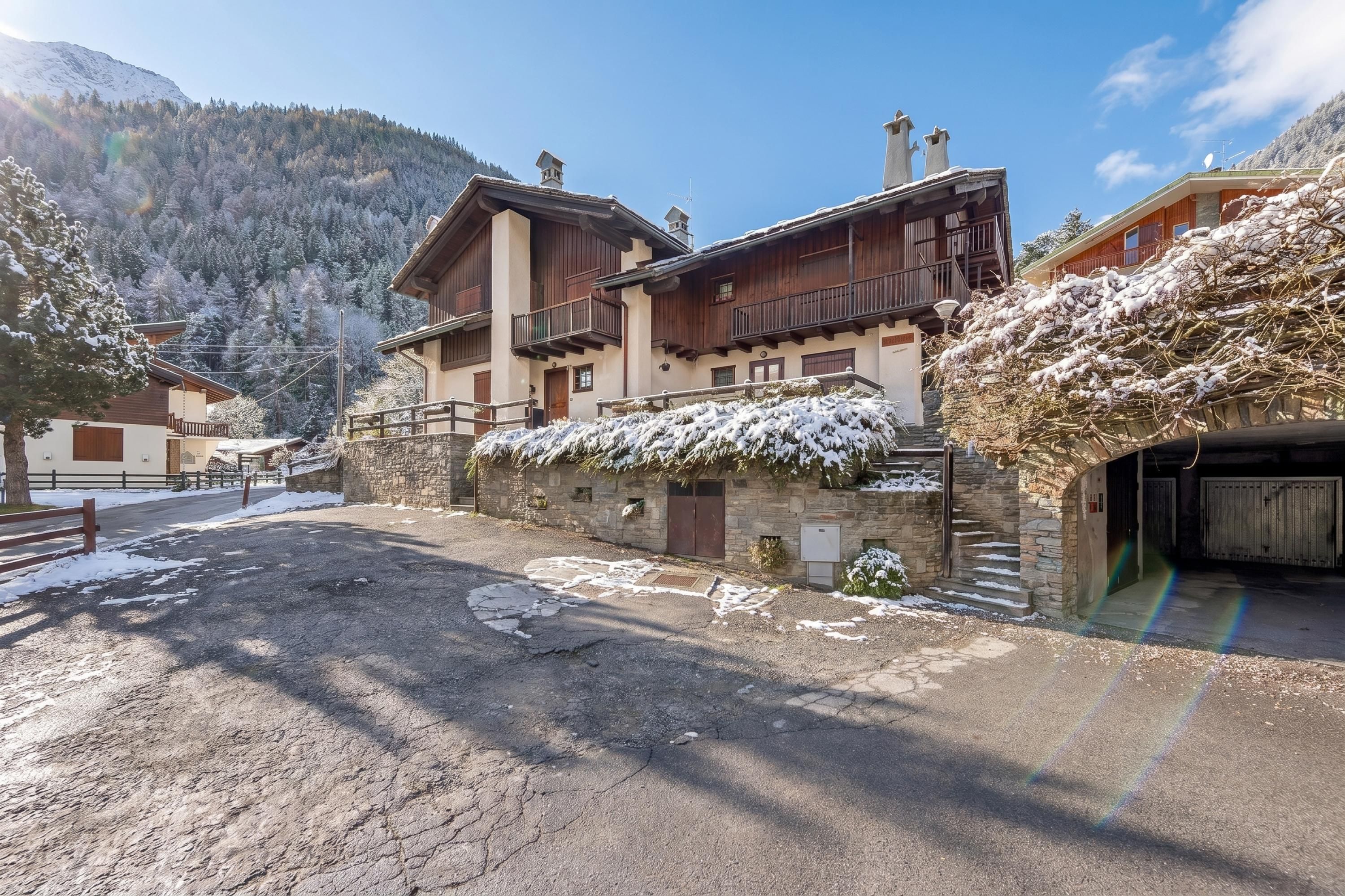 A two-story chalet with a stone facade, wooden balconies, and a snow-covered landscape.