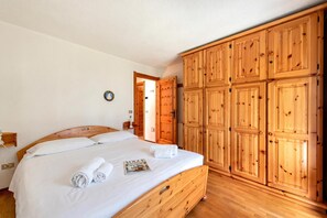 Une chambre à coucher avec un lit en bois, une armoire et une porte donnant sur une autre pièce.