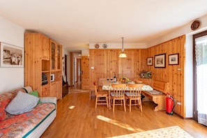 A wooden interior with a sofa, dining table, chairs, and a fire extinguisher. - Family Apartment Steps From Ski Lifts (Courmayeur)