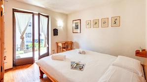 A hotel room with a bed, a wooden desk, a chair, a door with curtains, and a wall with framed pictures. - Family Apartment Steps From Ski Lifts (Courmayeur)
