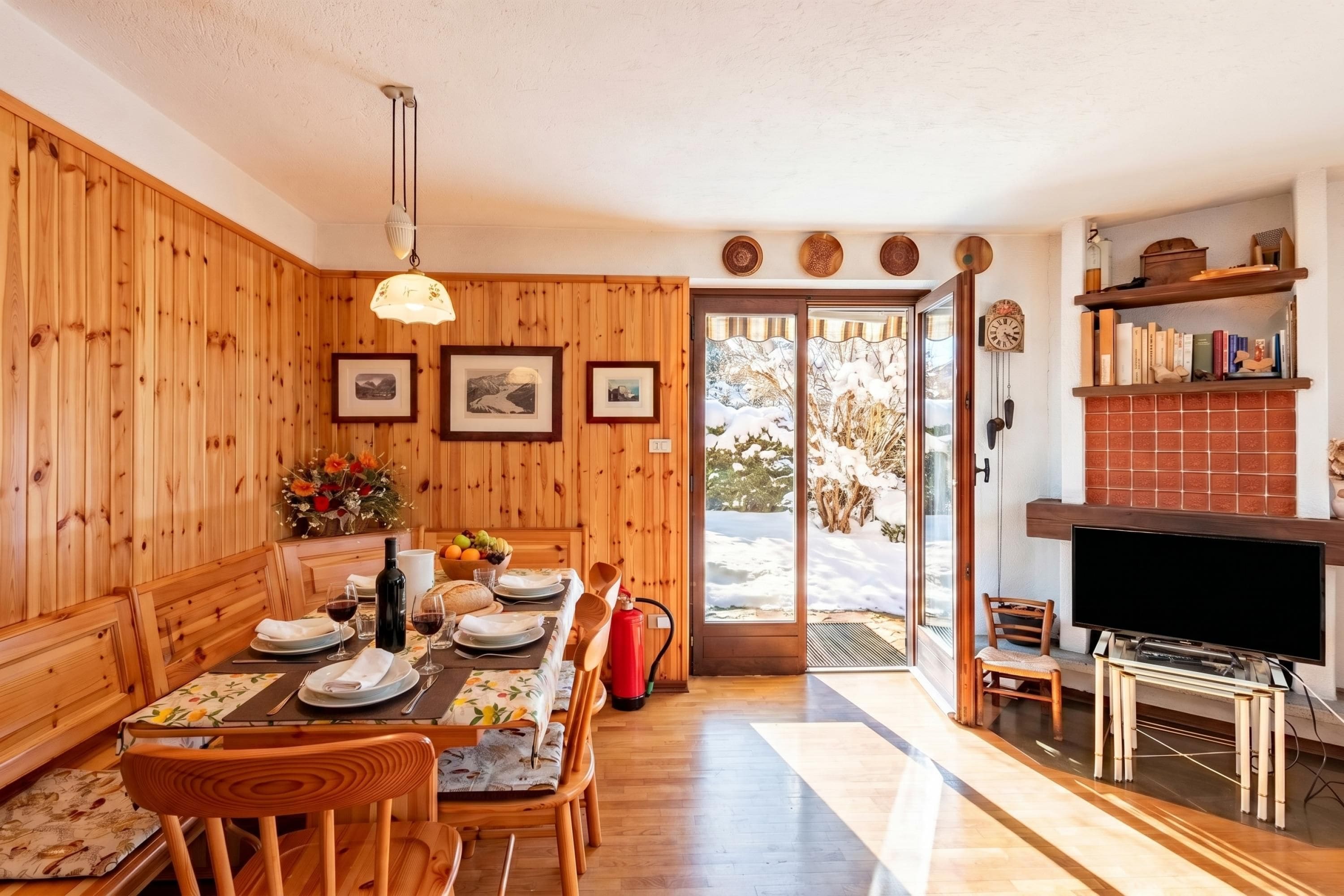 Un coin repas avec des murs en bois, une table dressée pour deux personnes et une cheminée sur laquelle est posée une télévision.