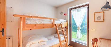 A bunk bed room with a wooden ladder, a desk, and a window with curtains.