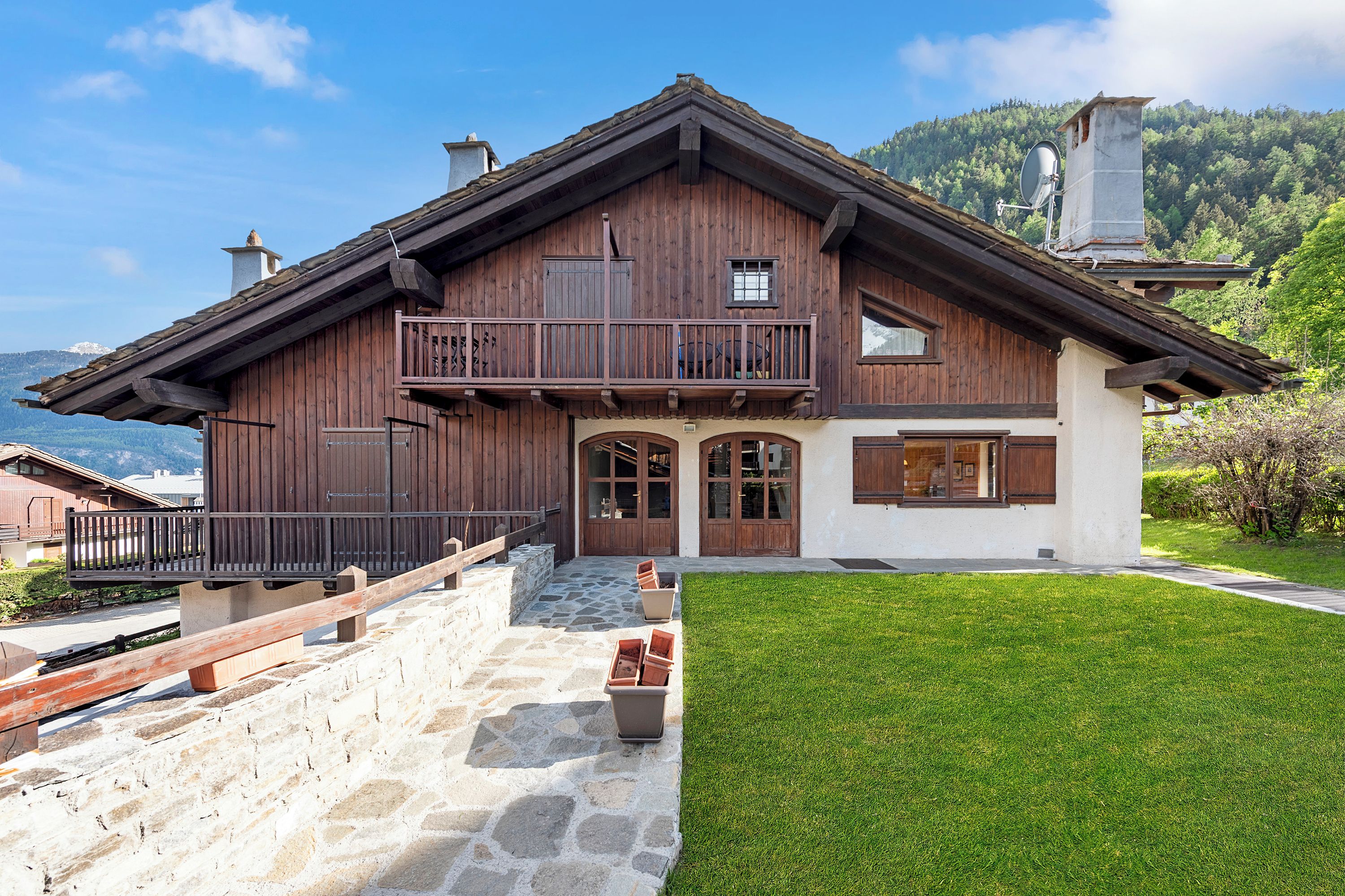 A wooden chalet with a balcony, stone steps, and a well-maintained lawn.