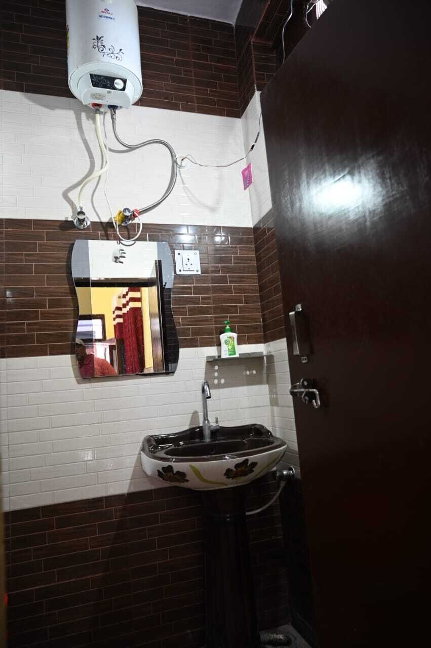 A bathroom with a white tiled wall, a black sink, a mirror, a towel rack, a heater, and a door.