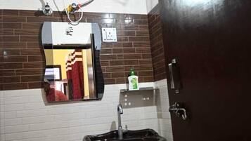 A bathroom with a white tiled wall, a black sink, a mirror, a towel rack, a heater, and a door.