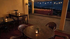 A dining area with round tables and chairs, potted plants, and string lights. - Hotel Kaushalya Residency (Berinag)