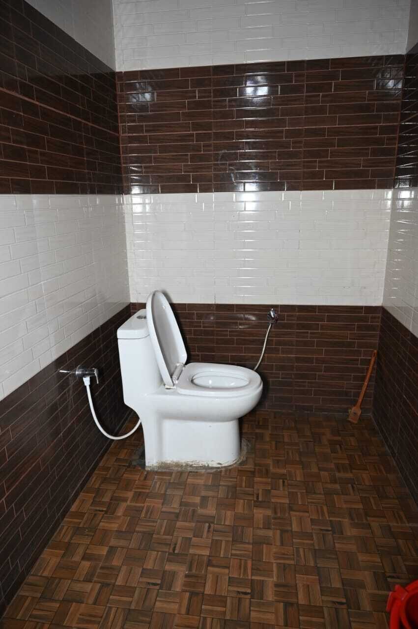 Un baño con inodoro blanco, paredes con azulejos marrones y blancos, y piso de madera.
