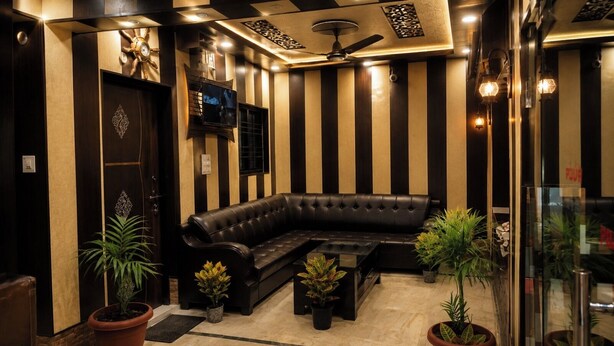 A modern lobby with a black leather sofa, potted plants, a wall-mounted TV, and a ceiling fan. - Hotel Kaushalya Residency (Berinag)