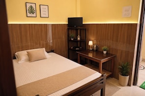 Habitación de hotel con cama, televisor, una mesita de noche con lámpara y una planta en maceta.