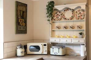 Eine Küche mit einem Vintage-Toaster, einer Mikrowelle, einem Wasserkocher und einem dekorativen Schrank mit floralen Tellern und Tassen.