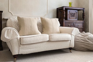 Ein cremefarbenes Sofa mit strukturierter Stoffoberfläche, platziert vor einer Wand mit dekorativer Friesenleiste.