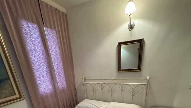 A neatly made bed with pillows and towels, a bedside table with a lamp, a window with curtains, and a framed picture on the wall. - Cozy apartment near the station (Venezia)