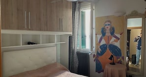 A bedroom with a bed, a radiator, a window, a shelf, and a painting on the wall. - Vrbo Property (Venezia)