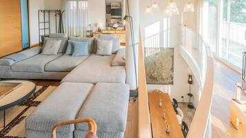 A modern living room with a grey sectional sofa, a wooden dining table, and a staircase leading to an upper level.