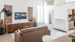 Ein modernes Wohnzimmer mit einer Couch, einem an der Wand befestigten Fernseher, einem Esstisch und einer Küche im Hintergrund.