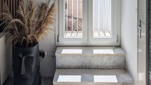 Ein moderner Eingangsbereich mit Doppeltüren, einem Blumentopf und Blick auf Gebäude durch die Fenster.
