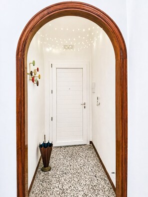 A hallway with a wooden archway, a white door, a wall-mounted light fixture, and a patterned floor. - La Tana della Volpe - Monopoli (Monopoli)