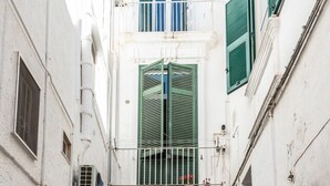 Eine enge Straße mit weißen Gebäuden, grünen Fensterläden und einem kleinen Balkon.