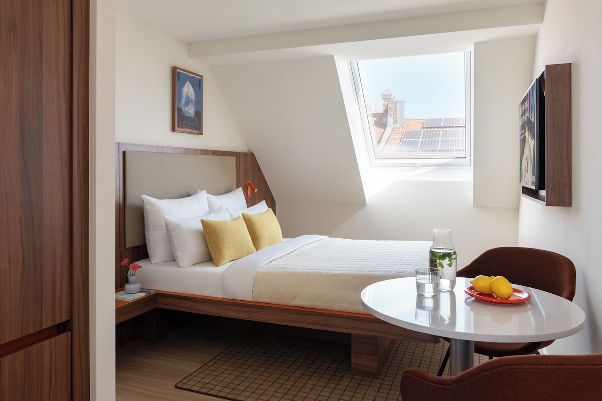 Een moderne hotelkamer met een hoogslaper, een eettafeltje en uitzicht op de stad door een dakraam.