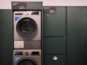 Ein Waschraum mit einer Bosch T1 Waschmaschine und einer HOS Waschmaschine, einem Schild für Wäschebedarf und einem Spender für schmutzige Handtücher.