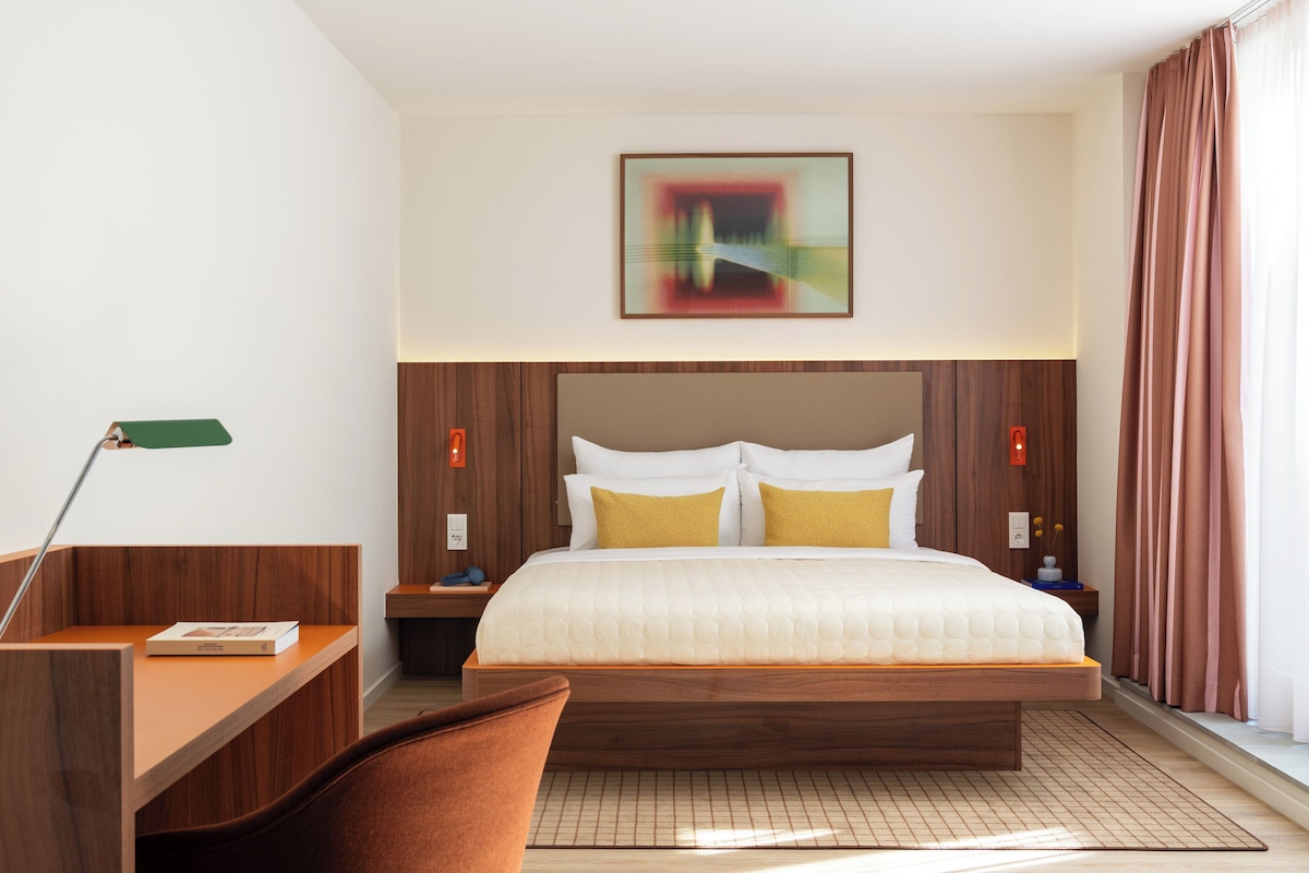 Een hotelkamer met een bed, een bureau, een stoel, een nachtkastje, een lamp en een schilderij aan de muur.