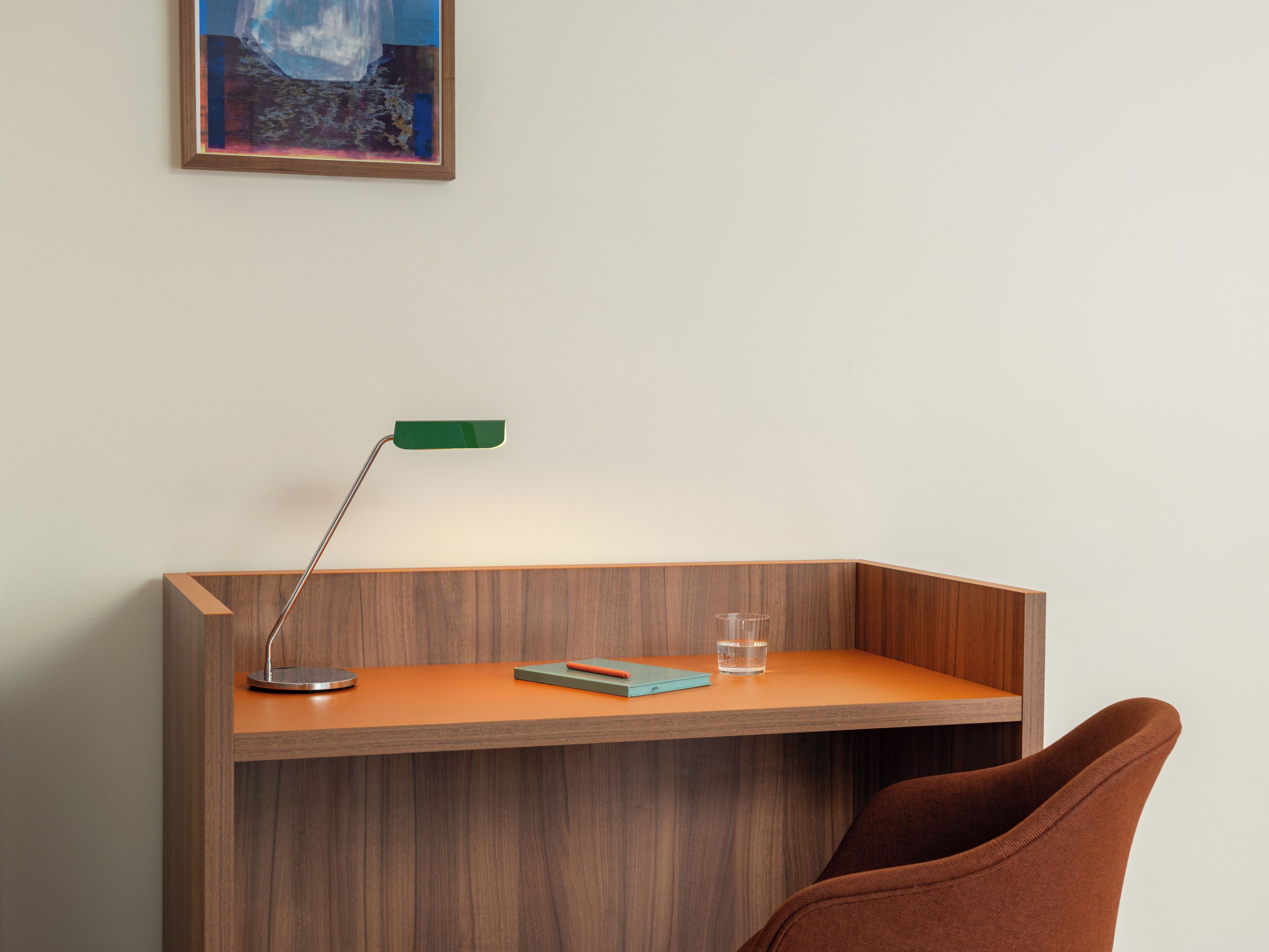 A desk with a lamp, a glass of water, and a notebook.