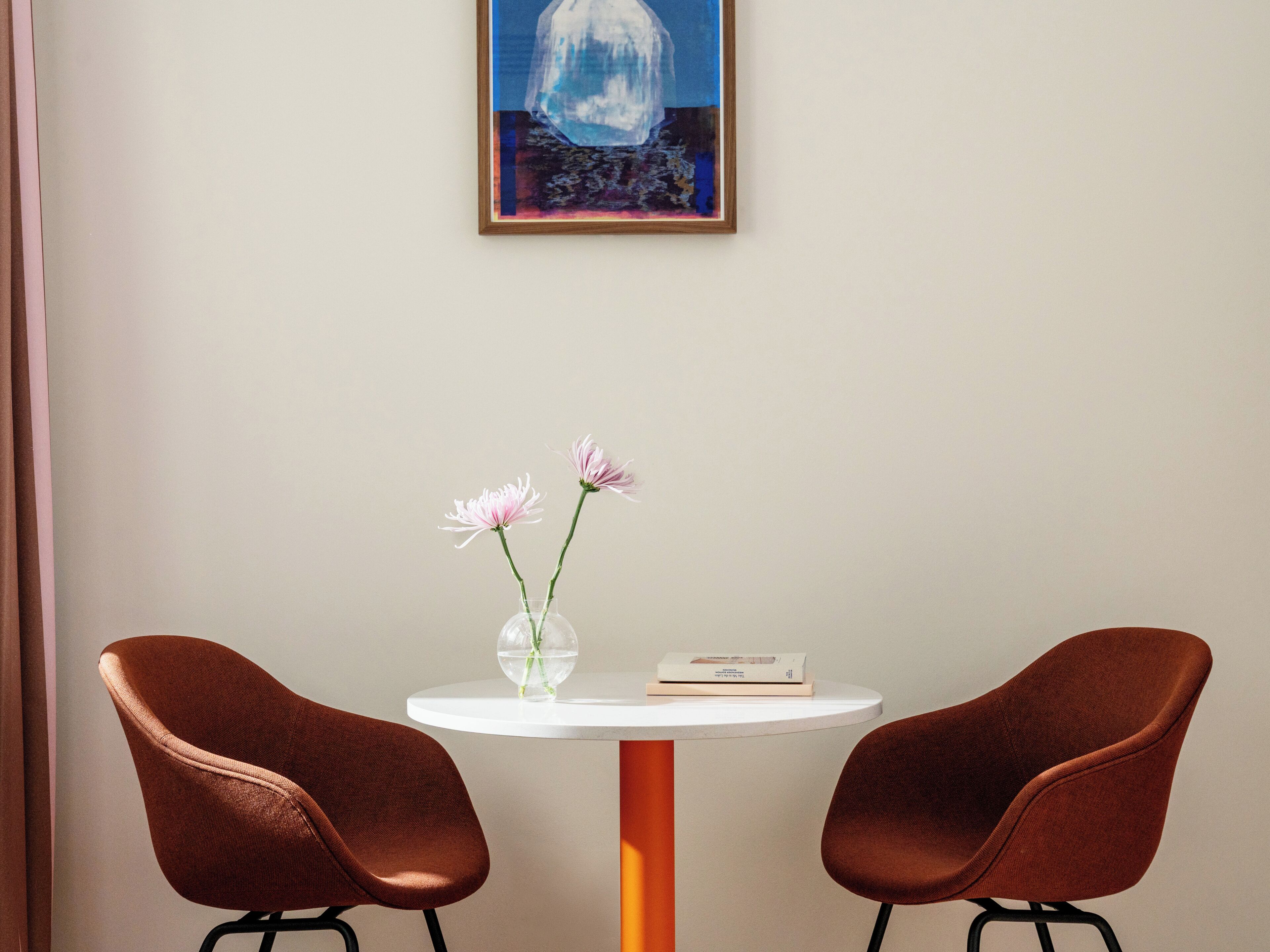 Ein Zimmer mit einem weißen Tisch, zwei braunen Stühlen, einer Blumenvase und einem gerahmten Gemälde an der Wand.