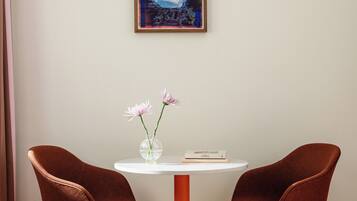 Ein Zimmer mit einem weißen Tisch, zwei braunen Stühlen, einer Blumenvase und einem gerahmten Gemälde an der Wand.